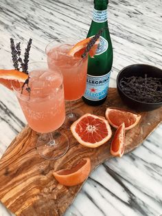 two glasses filled with orange juice and garnished with lavender sprigs on a wooden board