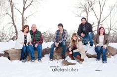 a group of people sitting on top of rocks in the snow with trees behind them