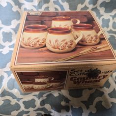 a box with four coffee mugs sitting on top of a blue and white tablecloth