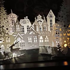 paper cut out of houses and trees with deers in the foreground at night