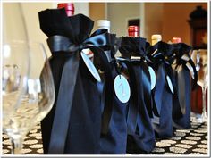 wine bottles and glasses are lined up on a table with black satin bags tied around them