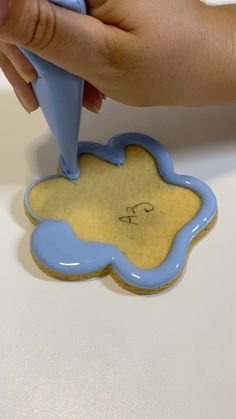 a cookie shaped like a cloud being held by someone's hand with a blue object in the shape of a flower