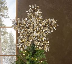 a small christmas tree with gold leaves and lights in front of a window on a table