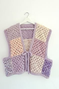 a crocheted vest hanging on a hanger, with multiple squares in pastel colors