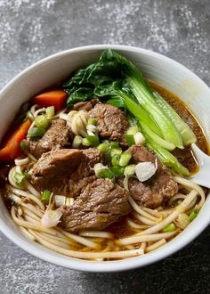 a white bowl filled with meat and noodles next to carrots, celery