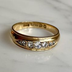 a gold wedding ring with five diamonds on it, sitting on a white marble surface