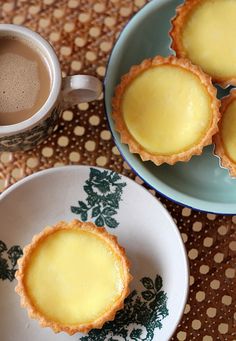 three small tarts on plates next to a cup of coffee and a plate with two cups