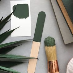 a brush and some green paint on top of a table next to a potted plant