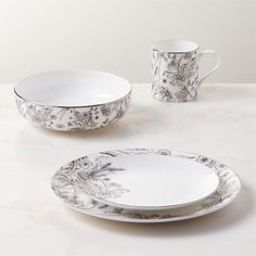 two white dishes with black floral designs on them, one has a cup and saucer