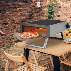 a pizza is being cooked in an outdoor oven on a table with chairs around it