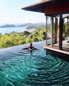 a woman is swimming in the water near a large pool with an open deck and glass doors