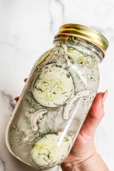 a person holding a mason jar filled with cucumber slices and dill pickles