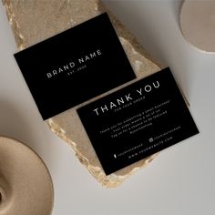 two black business cards sitting on top of a white table next to a cup and saucer