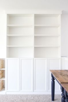 an empty white bookcase in the corner of a room next to a wooden table