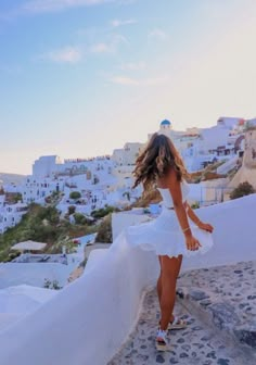 a woman in a white dress is walking up some steps with her hair blowing in the wind