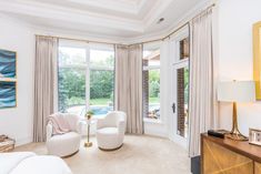 a living room with two white chairs and a table in front of large windows that look out onto the yard