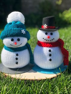 two knitted snowmen sitting on top of a piece of wood in the grass