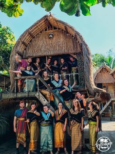 a group of people standing next to each other in front of a hut on stilts