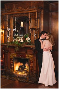 a man and woman standing next to each other in front of a fireplace