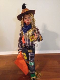 a little boy dressed up as a scarecrow with a trick on his face and holding an orange bag