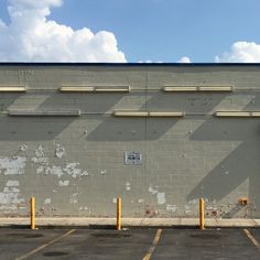 an empty parking lot in front of a gray brick building with yellow poles and windows