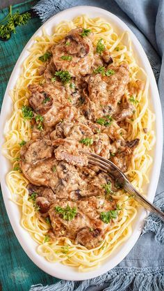 a white plate topped with pasta and meat covered in gravy next to a fork