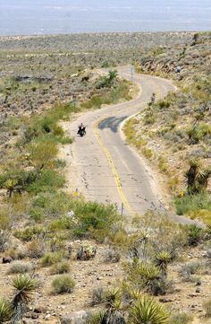 two motorcyclists riding down a road in the middle of an arid area