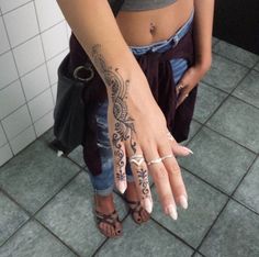 a woman with tattoos on her arm and hand is standing in front of a tiled wall