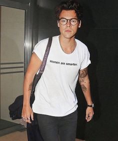 a man with glasses and a white t - shirt is standing in front of a door