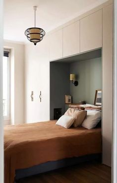 a bed sitting in a bedroom next to a window with a light hanging above it