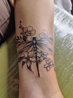 a woman's foot with a dragonfly tattoo on it and flowers around the ankles