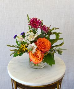 an arrangement of flowers sits on a marble table