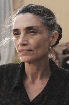 an older woman with dark hair and black shirt looking off to the side while standing in front of a building