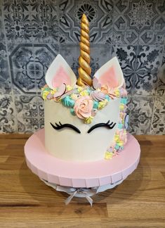 a white cake with pink icing and a unicorn horn on top, sitting on a wooden table