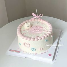 a white cake with pink frosting and a baby bear decoration on top, sitting on a table