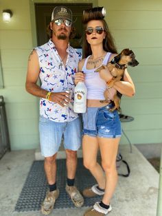 a man and woman are standing outside with their dog in front of the house, one is holding a bottle of booze