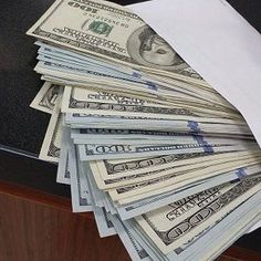 a stack of twenty dollar bills sitting on top of a desk next to a white envelope