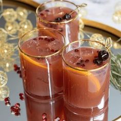 three glasses filled with liquid and garnished with berries sit on a glass tray