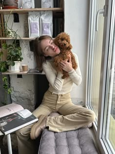 a woman sitting on a window sill holding a teddy bear in her hands and smiling