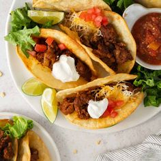 three tacos on a plate with salsa and sour cream