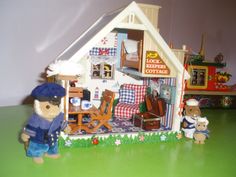 a toy house with two teddy bears in front of it on a green table top