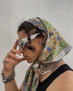 a woman wearing sunglasses and a scarf on her head holding something up to her eye