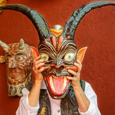 a man holding his face up to the camera while wearing a mask with large horns