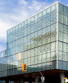 a large glass building sitting on the side of a road next to traffic lights and trees