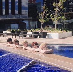 five people are sitting in the water at an outdoor swimming pool with their backs turned to the camera