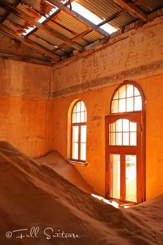 an empty room with two windows and sand piled on the floor