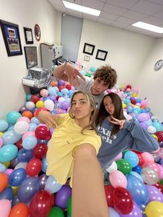 three people standing in a ball pit with balloons all around them and one person pointing at the camera