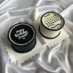 two black and white decorated cakes sitting on top of a table covered in silver cloth