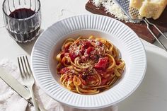 a white bowl filled with pasta and sauce on top of a table next to bread