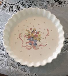 a white plate with flowers on it sitting on a doily next to a lace tablecloth